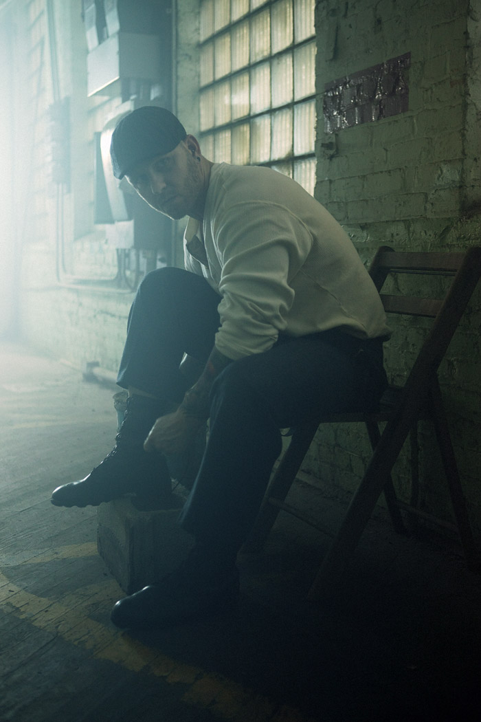 A man in a cap laces his boot by a glass-block window