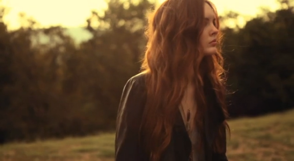 The model in a dark coat standing in a field at sunset
