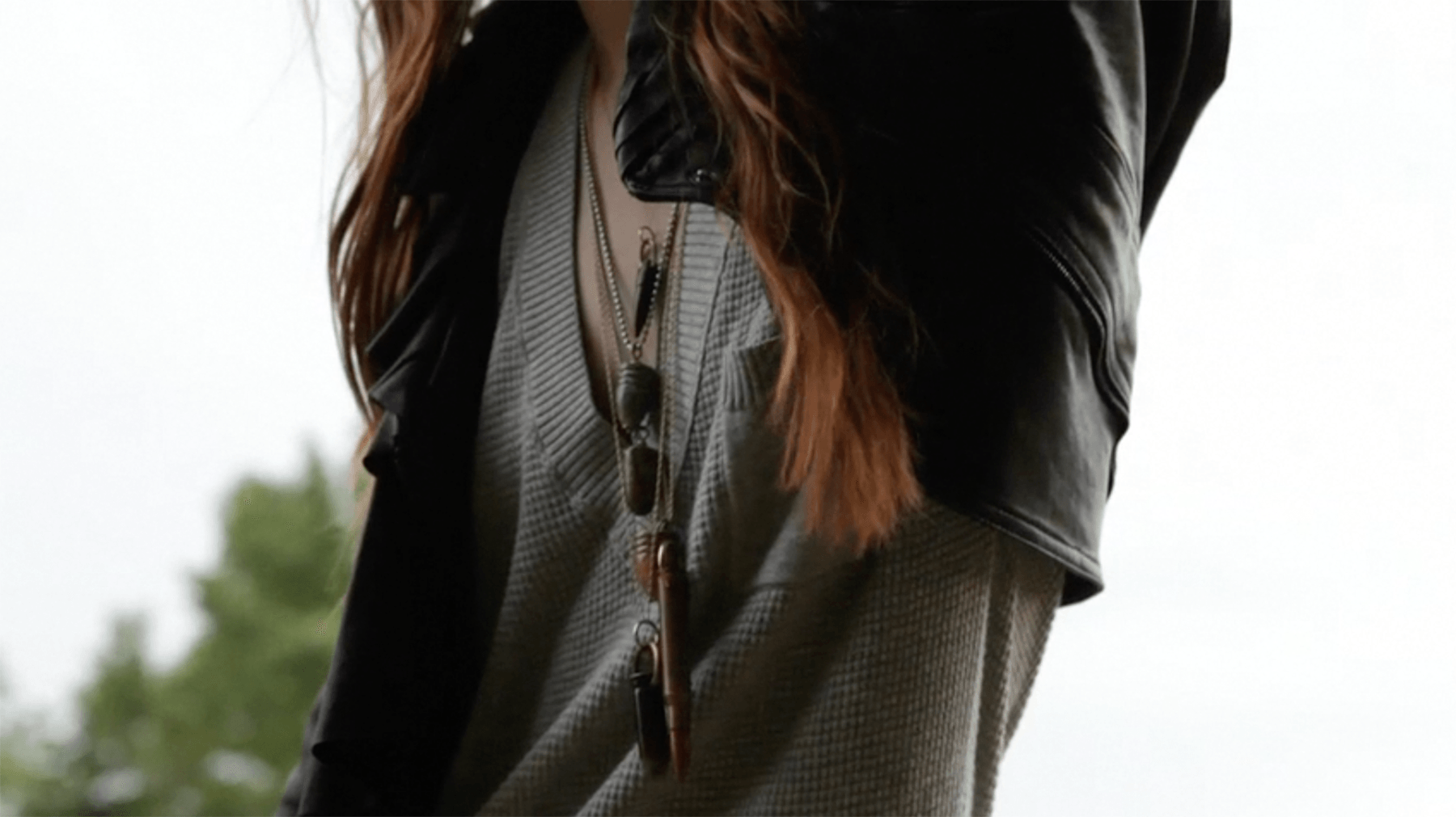 Bullet pendants on layered chains against a grey sweater