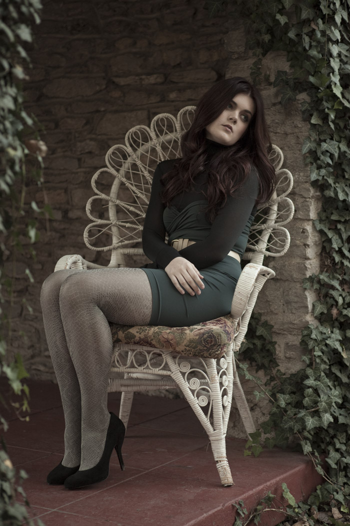 Model in a white peacock chair against an ivy wall